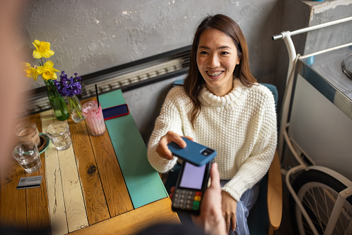 Female customer Japanese ethnicity paying her bill at the coffee shop, with mobile app via e-banking