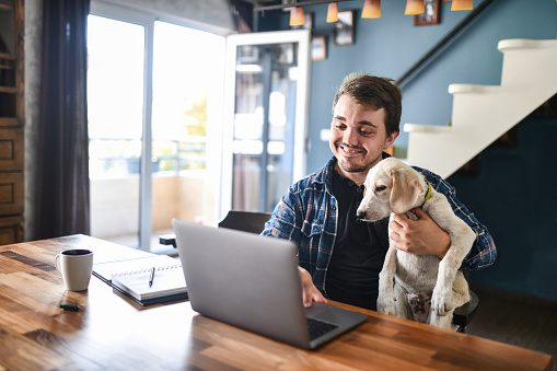 Disabled Male With Dwarfism Taking Notes From Online Clients And Holding Puppy While Working From Home