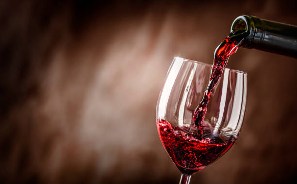 Pouring red wine into the glass against rustic background. stock photo