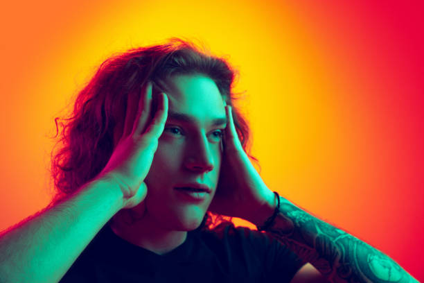 istock Young shocked man with long curly hair posing isolated on gradient orange-pink background in neon. Concept of beauty, fashion, youth culture and emotions 1400791908