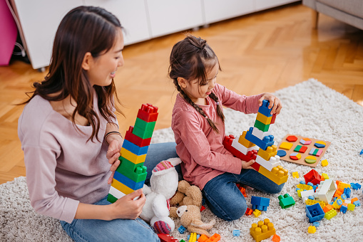 Young mother playing with her child on the rug on the floor with toys.