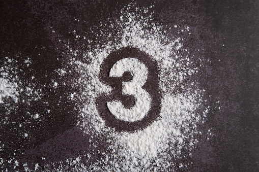The number 3 is written on scattered white flour through a stencil on the dark bacground