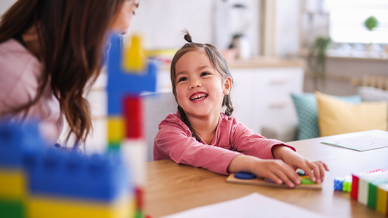 Young mother playing with her child on the kitchen table with toys.