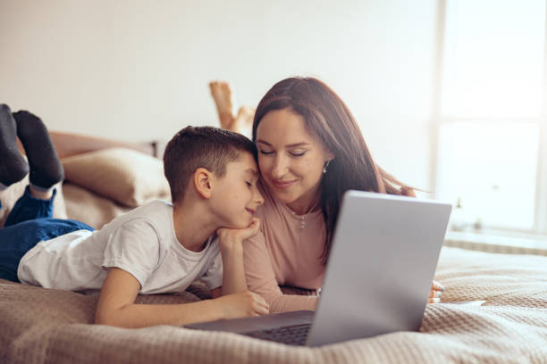 istock Happy Caucasian smiled mother and cute son cuddling while lying with laptop on bed. 1400794658