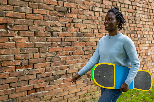 Side-view of urban young woman Black ethnicity holding a longboard