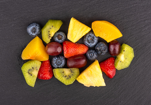 Berries and sliced fruits on a stone board for serving. Top view of fruit salad. Healthy eating.