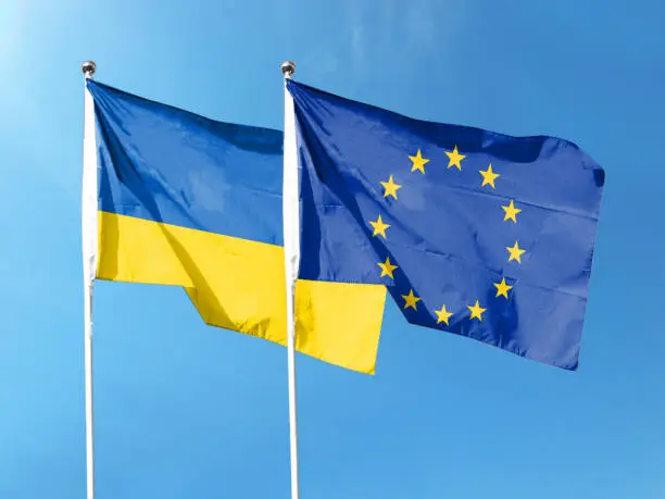 Photo of Flag of Ukraine and European Union flag with blue sky. waving blue sky
