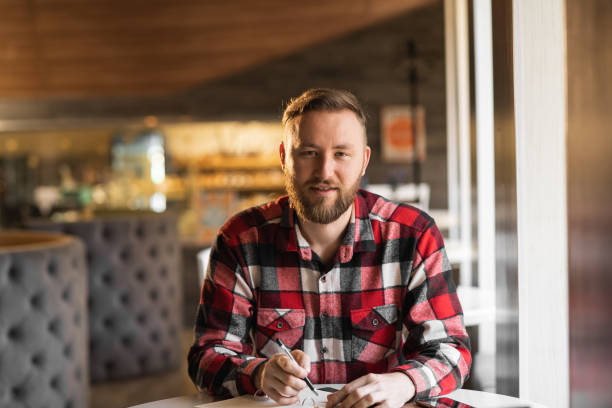 istock smiling bearded cafe owner planning work. male restaurant chef sits at the table after hours doing her bookkeeping in front of an camera. student search new idea inspiration in office cafe 1400799594