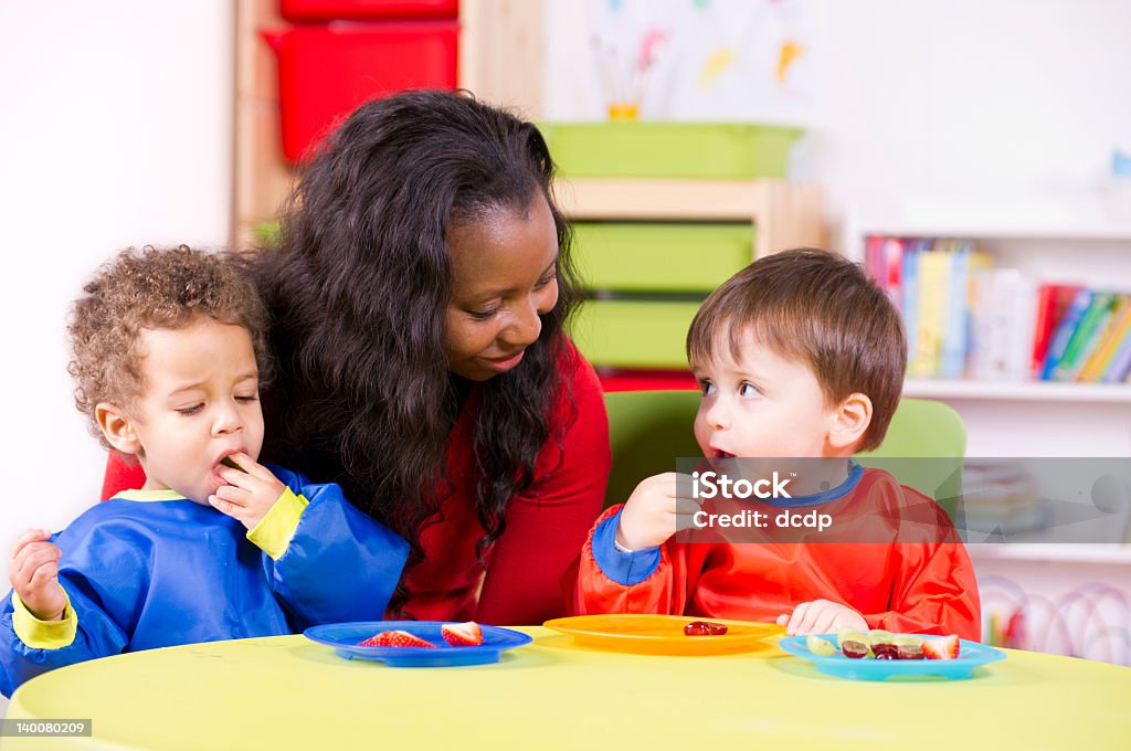 Children eating fruit at a nursery with their carer A stock photo of toddlers eating fruit and having a chat in the playroom. Child Care Stock Photo