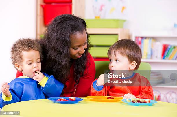 Children Eating Fruit At A Nursery With Their Carer Stock Photo - Download Image Now