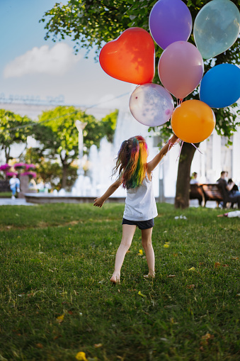 cute little caucasian girl with colourful dyed hair walking barefoot with bunch of baloons. Happy childhood and birthday celebration