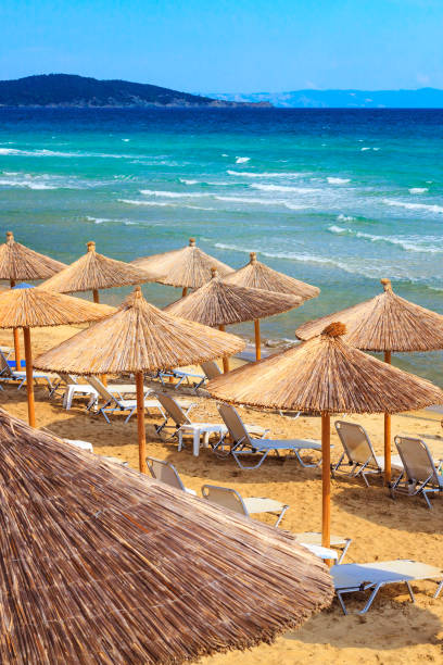 Sarti, Greece beach background with sea waves and umbrellas Halkidiki, Greece summer greek beach vacation panorama with turquoise sea water waves and umbrellas halkidiki stock pictures, royalty-free photos & images