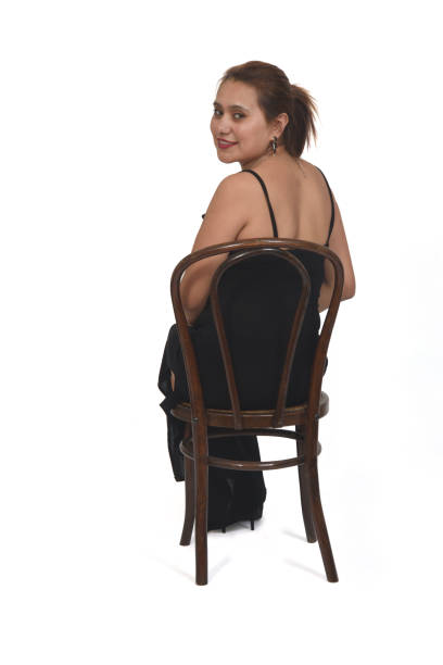 woman sitting on a chair who turns and looks at the camera dressed in a dress and high heels