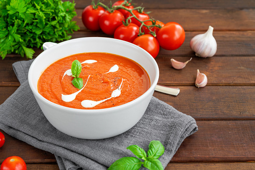 Tomato soup puree in a bowl with cream and fresh basil leaves on a dark wooden background. Copy space. Top view