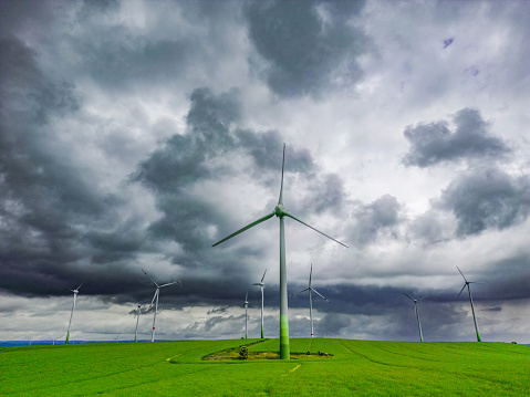 Drone point of view at wind turbines in front a upcoming storm with rainy clouds.