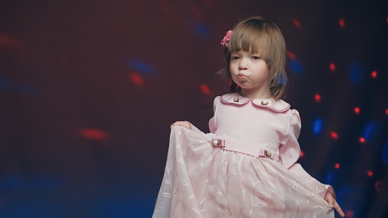 Cute little girl in vintage pink dress is spinning in dance and rejoicing. Concept of children theater productions and developing acting circles. Color music is shining and smoke is billowing