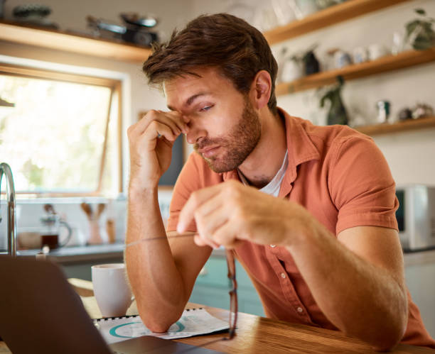 istock Young caucasian businessman suffering from a headache while working on a laptop from home alone. One stressed man looking unhappy while using a laptop. Person looking upset and worried 1400807217