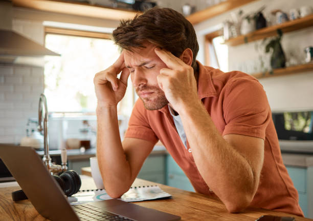 istock Young tired caucasian businessman suffering from a headache while working on a laptop from home alone. One stressed man looking unhappy while using a laptop. Person looking upset and worried 1400807223