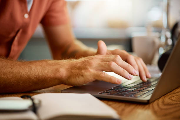 istock Man typing on a laptop while working from home alone. One businessperson working on a laptop and writing in a notebook while sitting at a table in the morning at home 1400807227