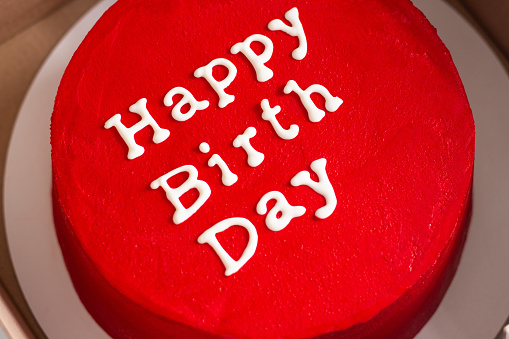 Birthday cake with lettering on top isolated on red. Red round birthday cake with an inscription wishing happy birthday in a box