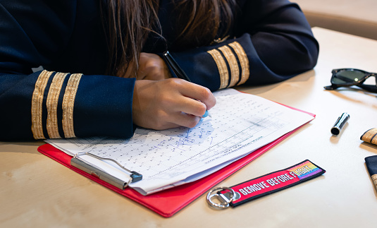 Unrecognizable female pilot preparing flight documentation with a Remove Before Flight keychain. High quality photo