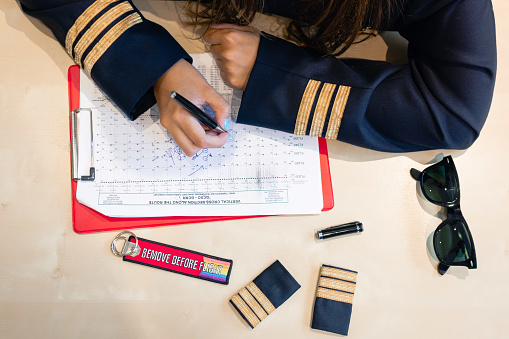 Unrecognizable female pilot preparing flight documentation with a Remove Before Flight keychain. High quality photo