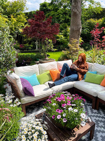 Stock photo showing ornamental Japanese-style garden with outdoor lounge area in Summer. Featuring a large expanse of white, interconnecting, white plastic decking tiles with outdoor patterned rug, providing a family space for outdoor hardwood, cushion covered seating.