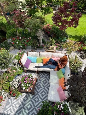 Stock photo showing ornamental Japanese-style garden with outdoor lounge area in Summer. Featuring a large expanse of white, interconnecting, white plastic decking tiles with outdoor patterned rug, providing a family space for outdoor hardwood, cushion covered seating.