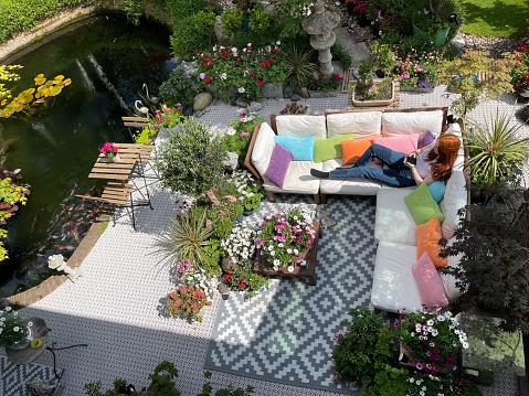 Stock photo showing ornamental Japanese-style garden with outdoor lounge area in Summer. Featuring a large expanse of white, interconnecting, white plastic decking tiles with outdoor patterned rug, providing a family space for outdoor hardwood, cushion covered seating.