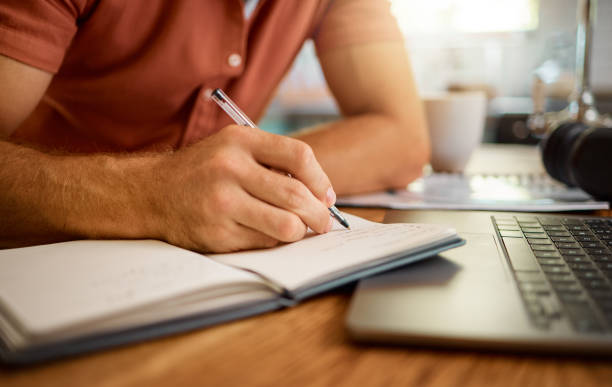 istock Man writing in a diary while working from home alone. One businessperson working on a laptop and writing in a notebook sitting at a table in the morning at home 1400815980