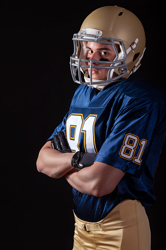 Young football player standing with arms folded looking tough on black background