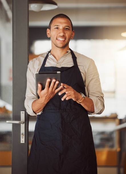 istock Businessman using a digital tablet in his cafe entrance. Bistro boss using an online app in the restaurant. Young small business owner using a wireless digital device in his cafe. 1400817963