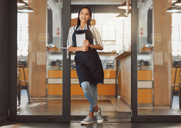 Portrait of businesswoman standing in coffeeshop entrance. Business owner holding a digital tablet in her shop. Entrepreneur standing in entrance of her restaurant. Store owner using wireless device retrato de una mujer de negocios de pie en la entrada del coffeeshop. dueña de un negocio sosteniendo una tableta digital en su tienda. empresaria de pie en la entrada de su restaurante. propietario de la tienda con dispositivo inalámbrico