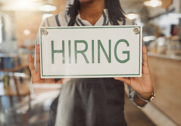 mains du propriétaire de l’entreprise tenant une pancarte d’embauche. femme d’affaires accrochant une pancarte d’embauche à l’entrée du café. patron annonçant que les rh embauchent du personnel. un propriétaire de petite entreprise accroche - hire photos et images de collection