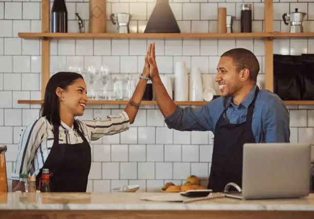 Business partners high five each other. Happy colleagues motivate each other in a shop. Restaurant owners collaborate and celebrate together. Entrepreneurs celebrate their coffeeshop success