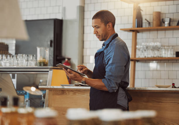 istock Mixed race businessman ordering stock on his digital tablet. Boss using a wireless device in his restaurant. Barista placing an online order on an app. Manager holding a digital device 1400817995