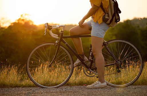 Woman cycling on a road with a mountain background and sunset.