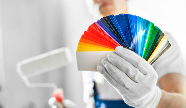 Painter man with paint roller and color palette, on painted wall background, stock photo