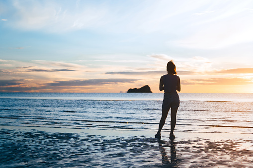 On summer vacation rear view of young adult tourist asian woman relax in nature on beach sea with beautiful dramatic twilight morning sky. Outdoor domestic travel at Hua hin, Thailand.