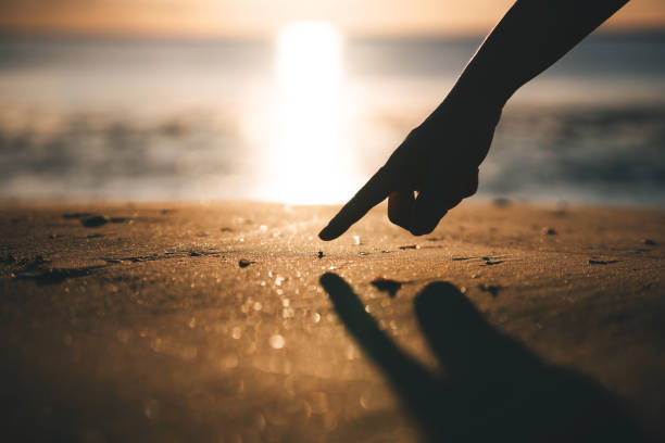 Human hand point to tiny cute crab on the beach sand. Positive emotion outdoor in nature with sunrise and bokeh background.