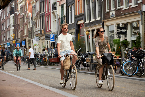 Shopping street with people riding bikes on the Haarlemmerdijk at summer sunset, Amsterdam, The Netherlands.