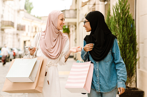 Two smiling young muslim women walking on a street carrying shopping bags