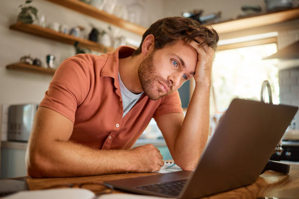 istock Young serious caucasian businessman working on a laptop from home alone. One stressed businessman looking unhappy while using a laptop. Person looking upset and worried 1400820534