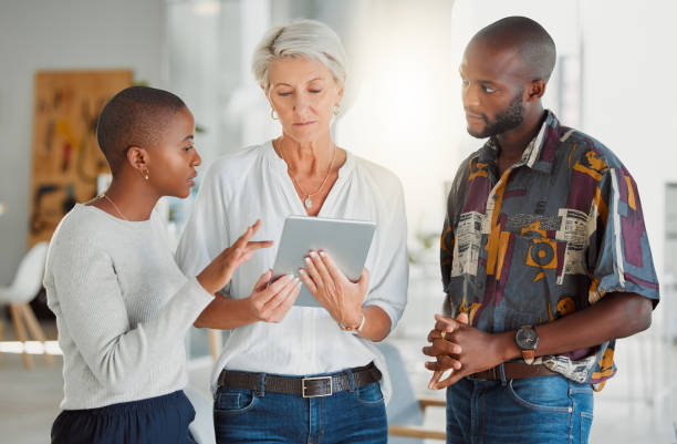 istock Three focused businesspeople using a digital tablet together at work. Mature caucasian businesswoman talking and showing her african american coworkers an idea of a digital tablet in an office 1400820552