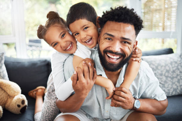 Portrait of a mixed race father,son and daughter bonding together at home. Hispanic boy and girl hugging and holding their father while smiling on the sofa in the lounge. Portrait of a mixed race father,son and daughter bonding together at home. Hispanic boy and girl hugging and holding their father while smiling on the sofa in the lounge. single father stock pictures, royalty-free photos & images