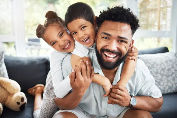 Portrait of a mixed race father,son and daughter bonding together at home. Hispanic boy and girl hugging and holding their father while smiling on the sofa in the lounge.