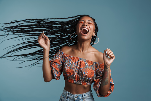 Young black woman with pigtails screaming while posing at camera isolated over blue background