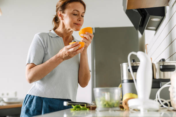 istock Ginger mature woman smelling orange while cooking in kitchen 1400823463