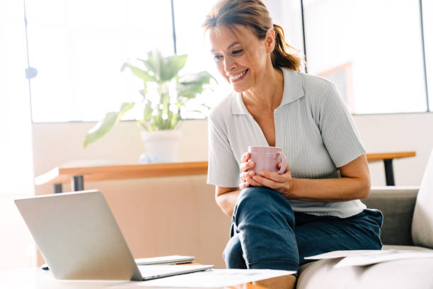 istock Ginger mature woman drinking coffee while working with laptop at home 1400823932