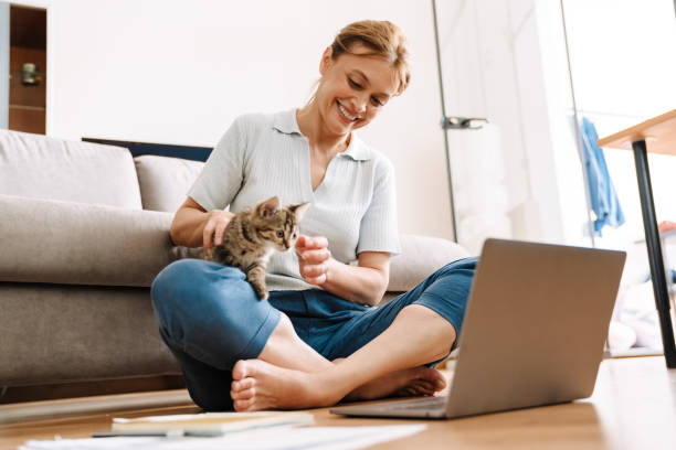 istock Ginger mature woman playing with her kitten while using laptop on floor 1400824314